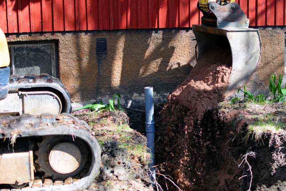 Excavator in construction site filling the sewer pipe trench with sand.